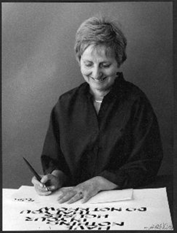 Motiv: Kalligrafen Else Marie Frandsen siddende ved et bord i færd med at kalligrafere på et stort ark papir